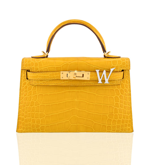 Yellow crocodile-patterned handbag with a gold clasp and white letter 'W' on a white background, collection-preview