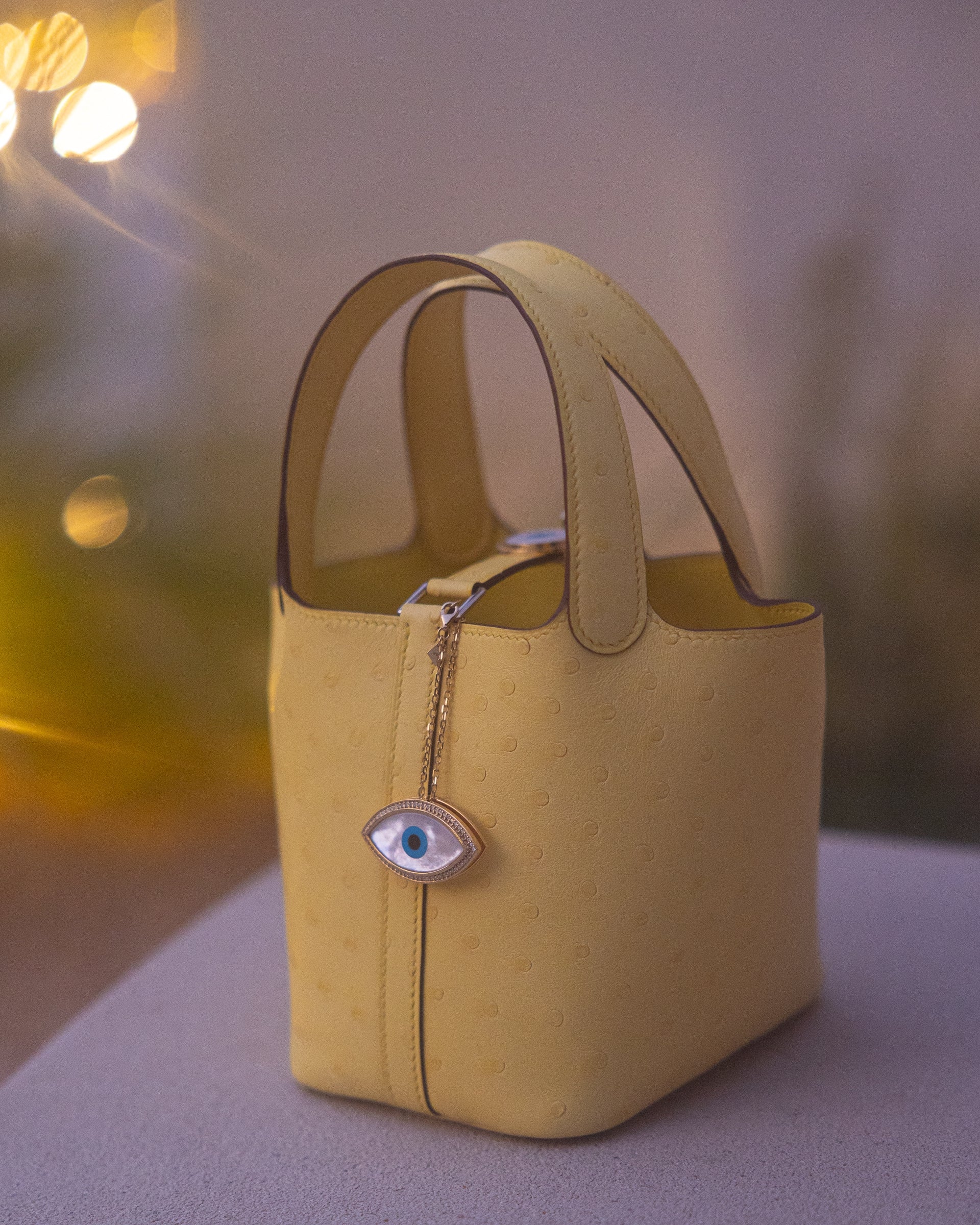 Yellow handbag with a decorative chain and evil eye charm 