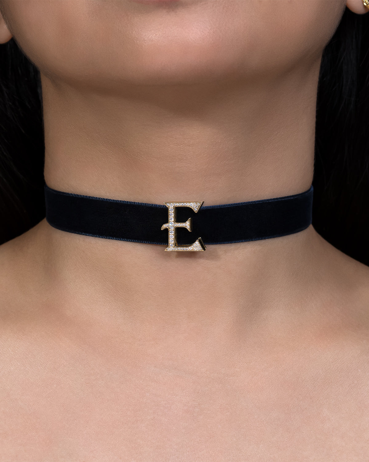 Black choker necklace with a gold 'E' clasp on a person's neck.