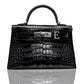 A black handbag with a crocodile pattern, featuring a metallic clasp and a leather handle, collection-preview.