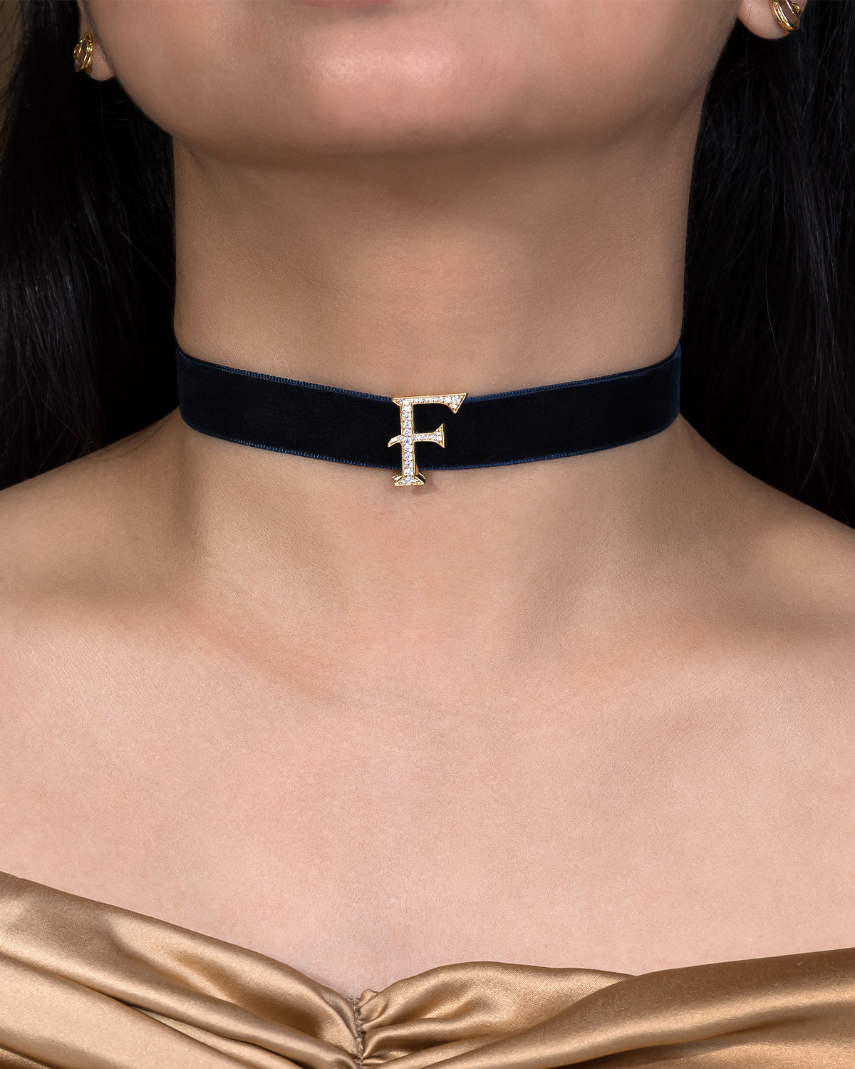 Black velvet choker with a gold 'F' pendant on a model wearing a gold top.
