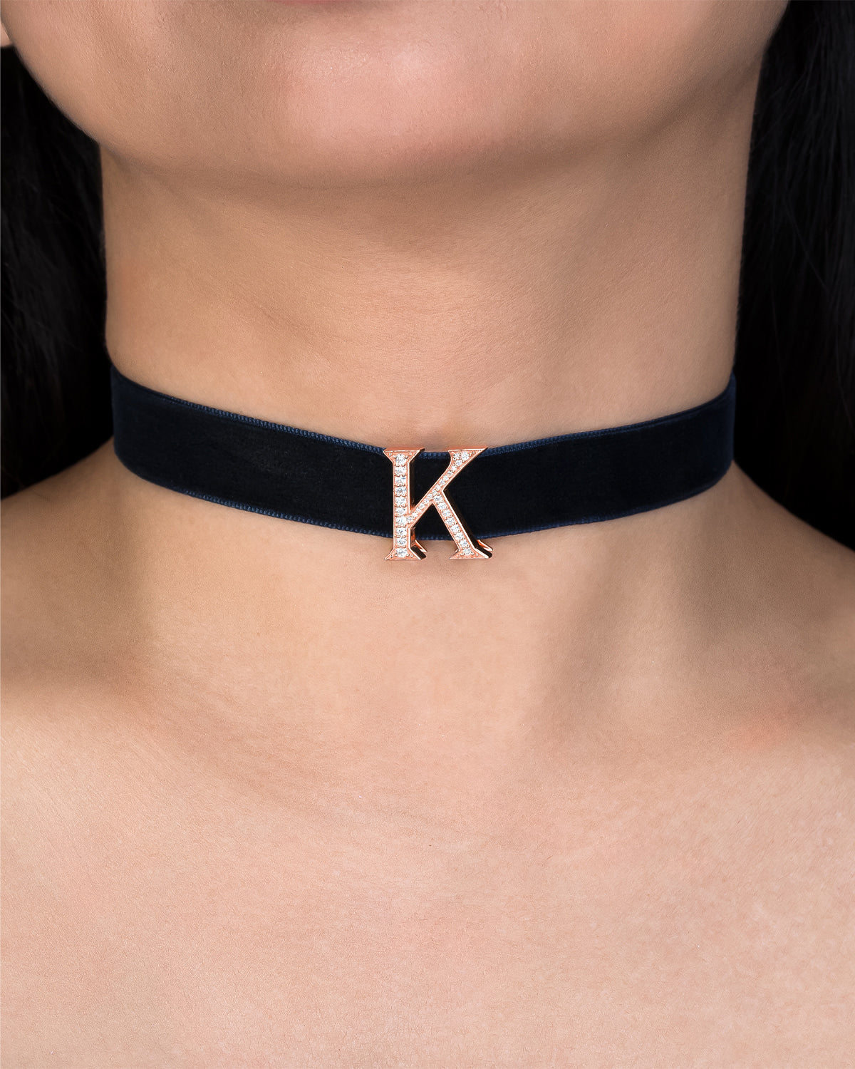 Navy blue velvet choker with a rose gold letter 'K' on a person's neck.