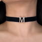 Black choker with a gold 'M' pendant on a person's neck