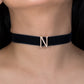 Black choker necklace with a letter 'N' pendant on a person's neck.