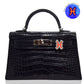 Black crocodile-patterned handbag with a distinctive clasp on a white background, collection-preview