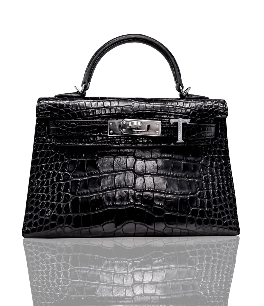 A black handbag with a crocodile pattern and a metallic 'T' closure, collection-preview.
