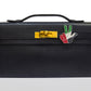 A black handbag with a metallic clasp and a decorative pin featuring geometric shapes and the colors red, green, and white. collection-preview.